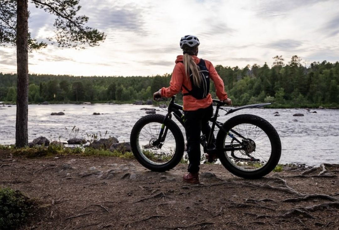 Pyöräilijä pysähtyneenä joen rantaan ihailemaan kauniin karua maisemaa.