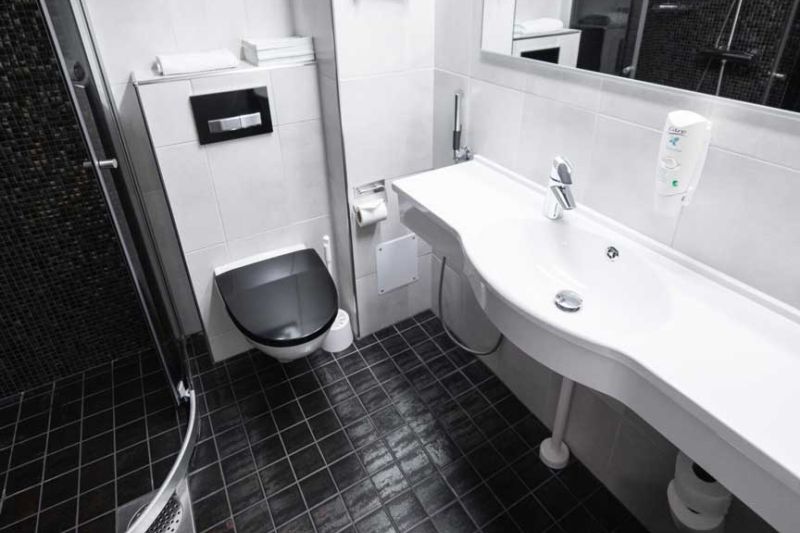 Valkea, mustalattiainen kylppäri wc-istuimella ja pitkällä allastasolla.