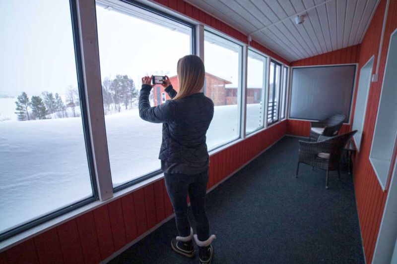 Nainen ottaa kuvaa kännykällä parvekkeen lasien läpi avautuvasta järven talvimaisemasta.