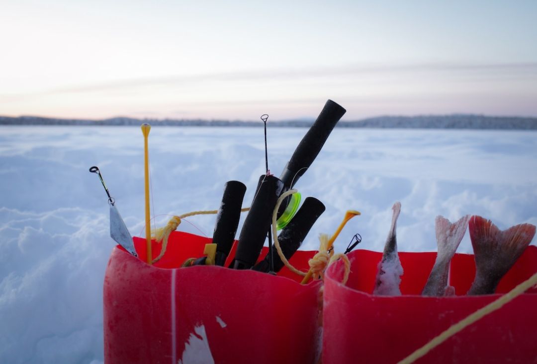 Ice fishing equipment on a red bucket on top of arctic lake in Inari Lapland Finland Snowy landscape. Photo by Miika Leivo.