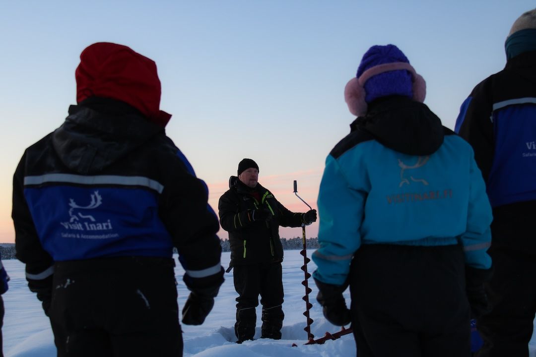 Fisher giving ice fishing instructions for visitors on top of arctic frozen laki in Inari lapland Finland. Photo by Miika Leivo.