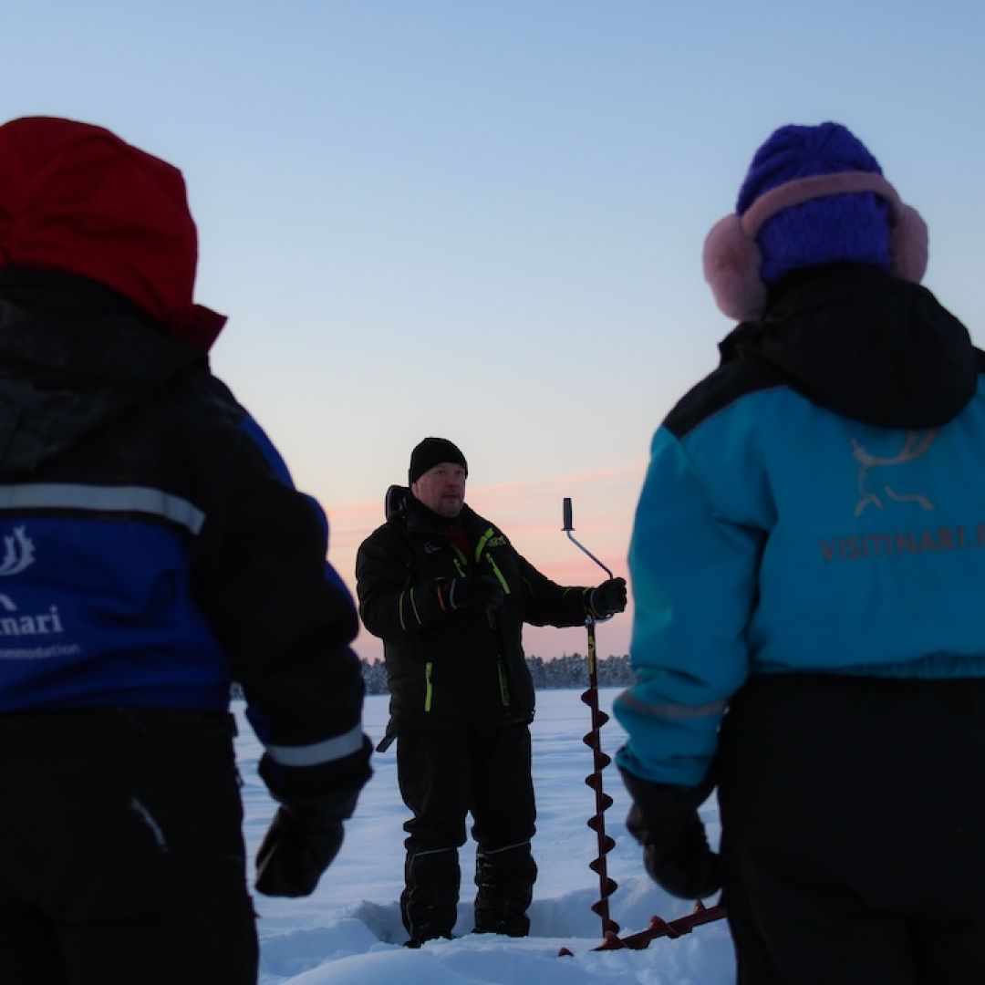 Fisher giving ice fishing instructions for visitors on top of arctic frozen laki in Inari lapland Finland. Photo by Miika Leivo.