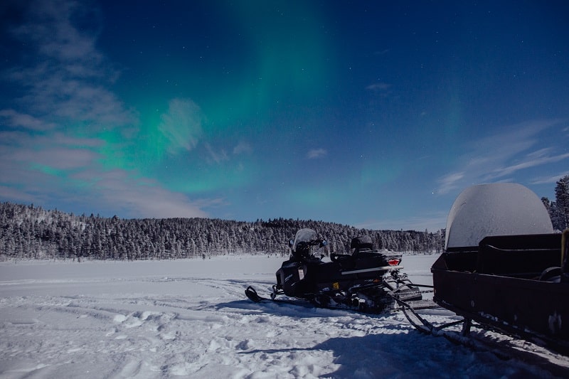 Snowmobile and sledge on frozen lake. Northern lights in the sky.
