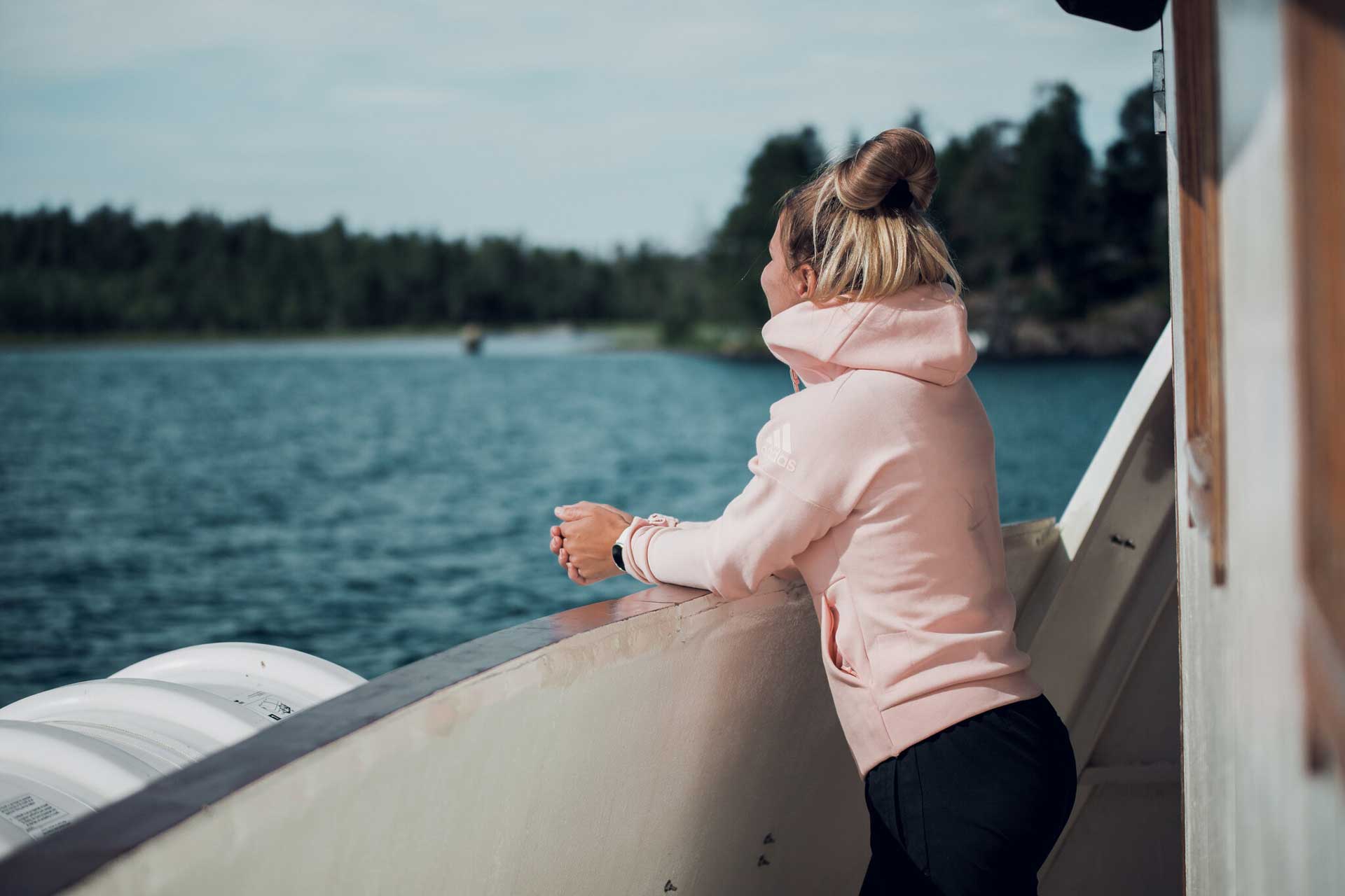 Woman in hoodie on a boat watching views.