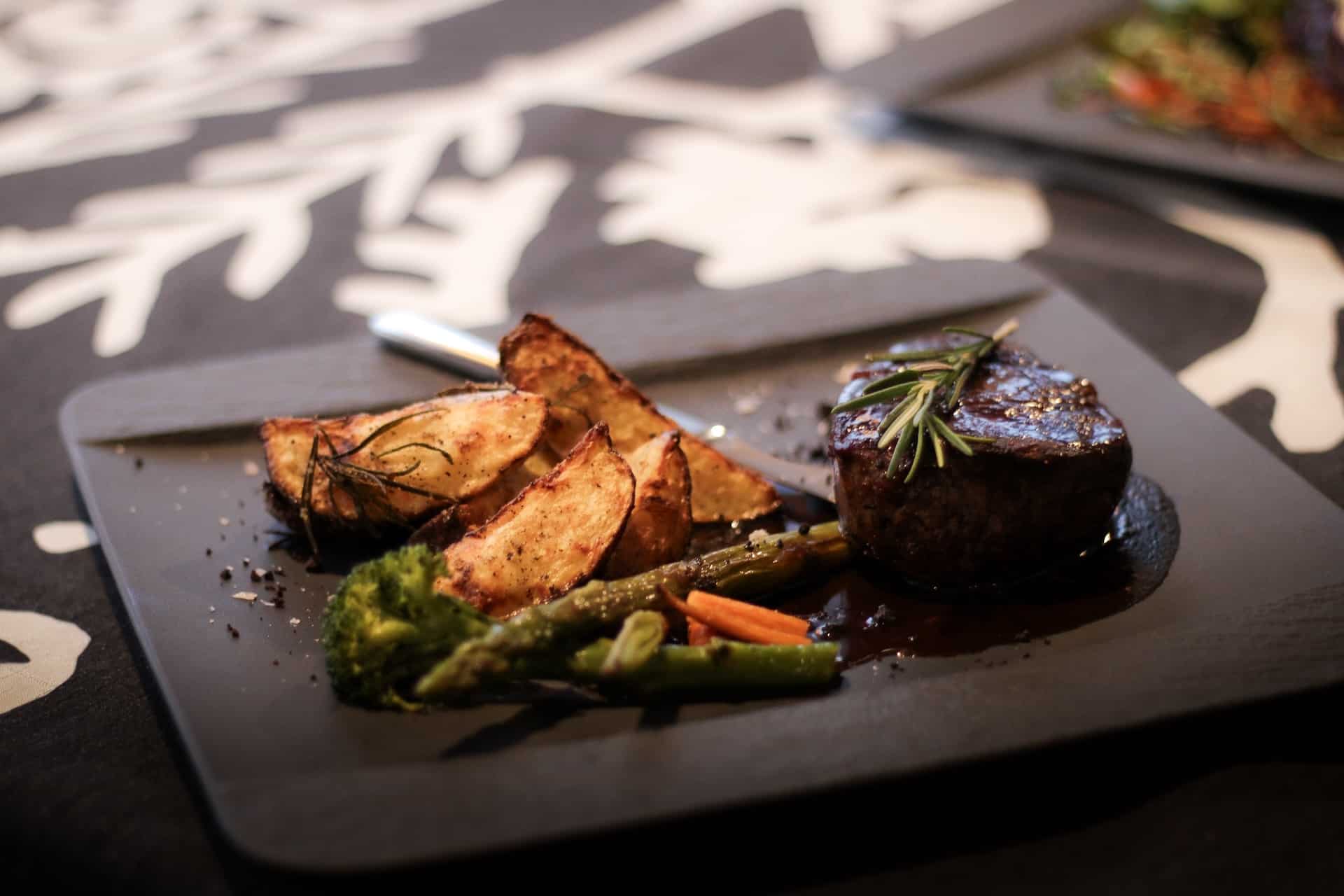 Restaurant Aurora dish on a plate. Dish includes round piece of meat, asparagus and roasted potato chips.