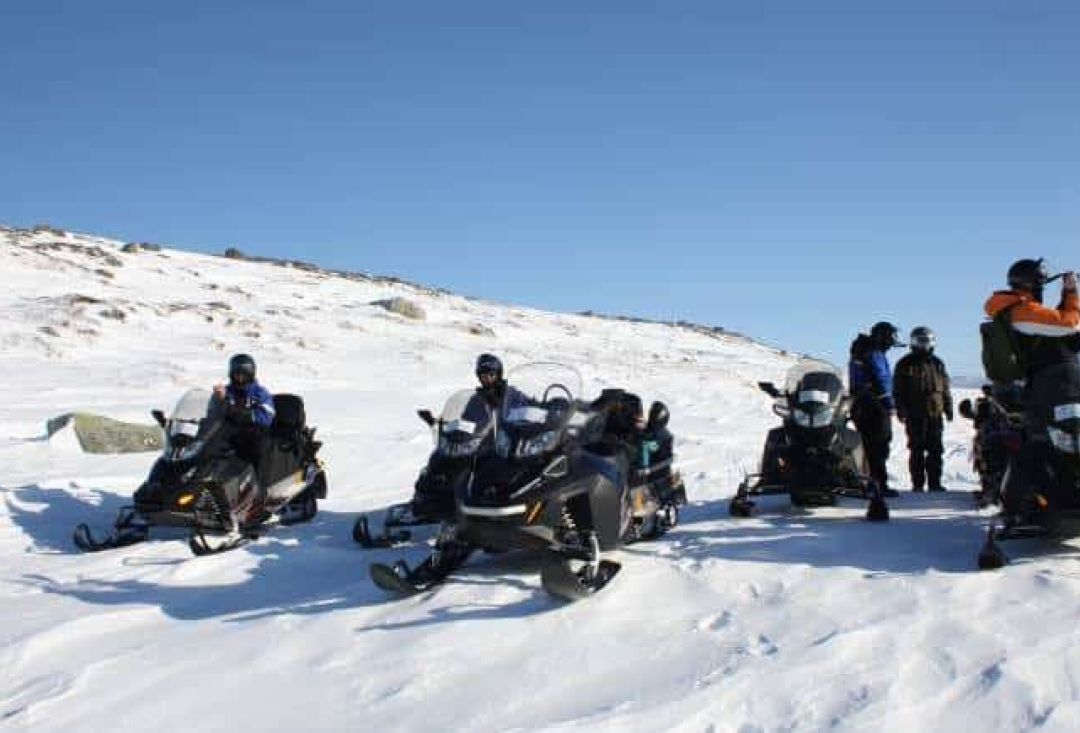 Group of snowmobile riders taking a break on a hill.