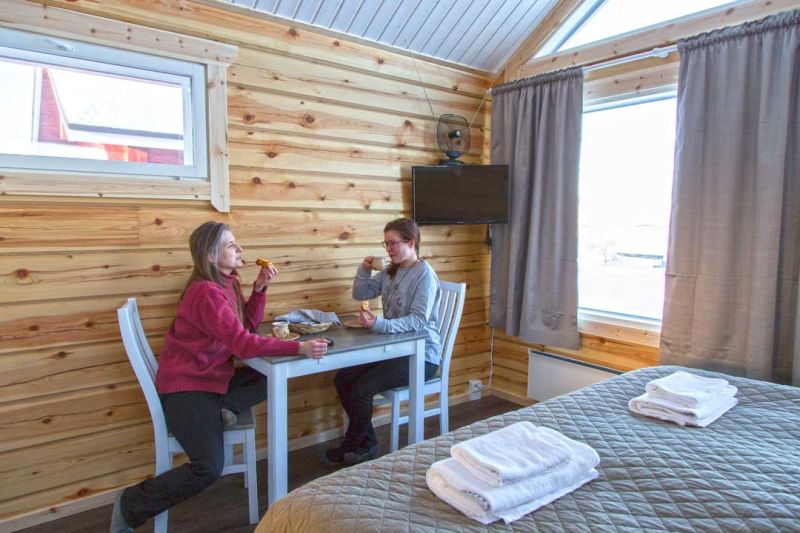 Kaksi naista istuu puisen seinän vieressä olevan pöydän ääressä syömässä. 