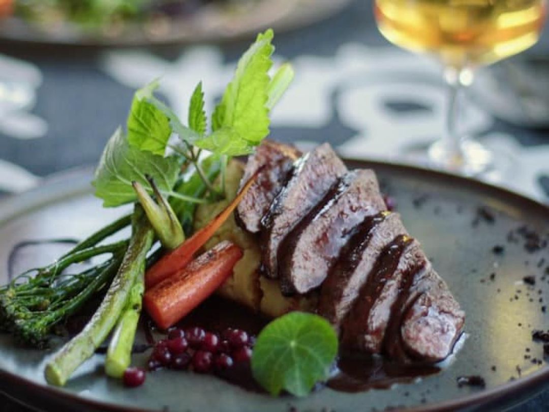 Gourmet-annos viipaloidusta lihasta, vihanneksista ja koristeista mustalla lautasella.