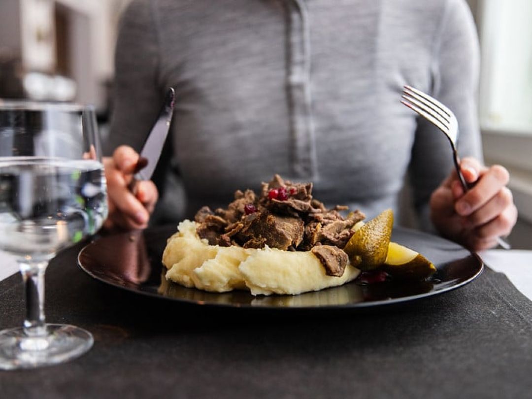 Henkilö aloittamassa ateriaa, jossa on perunamuusia, lihaa ja koristeita.