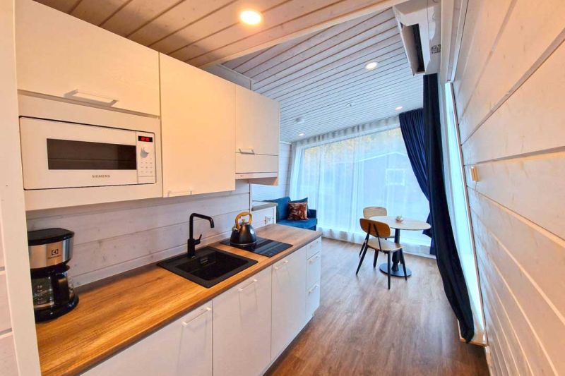White kitchen with wooden countertop. Equipped with coffee maker, sink, microwave and electric kettle.