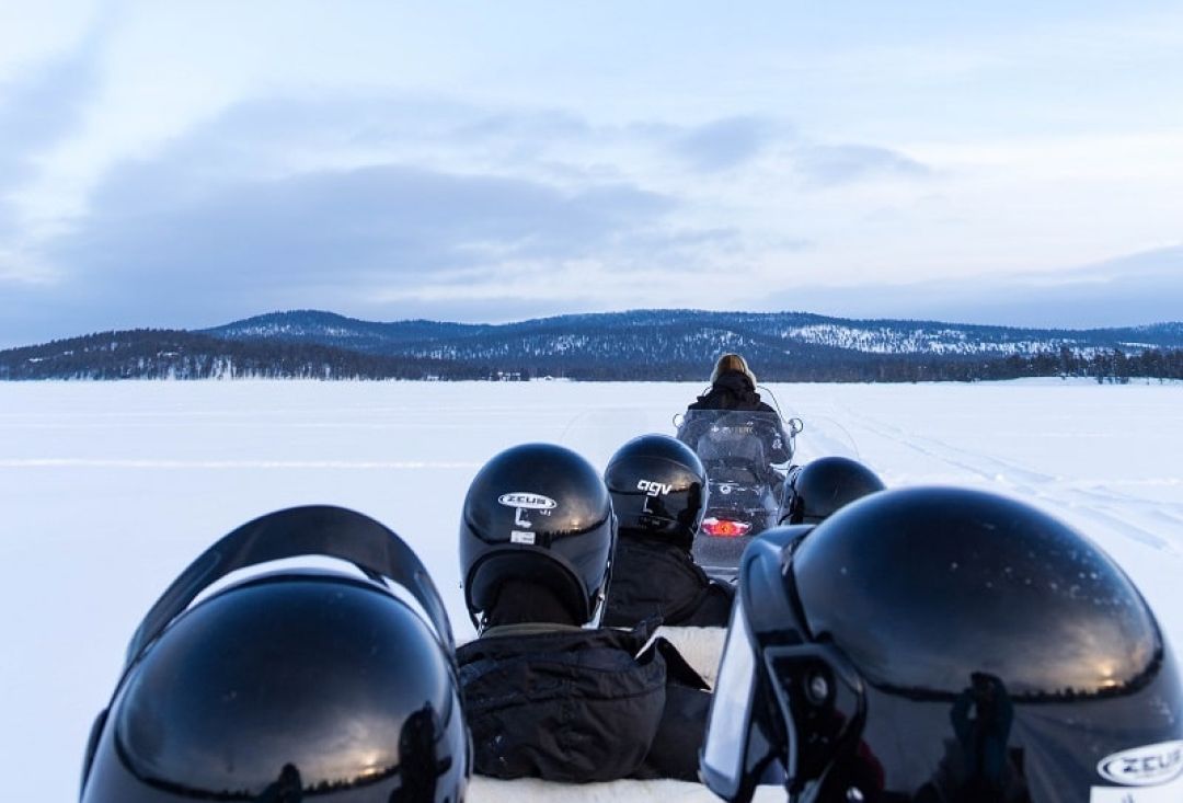 Many passengers sitting on snowmobile sledge with their helmets on.