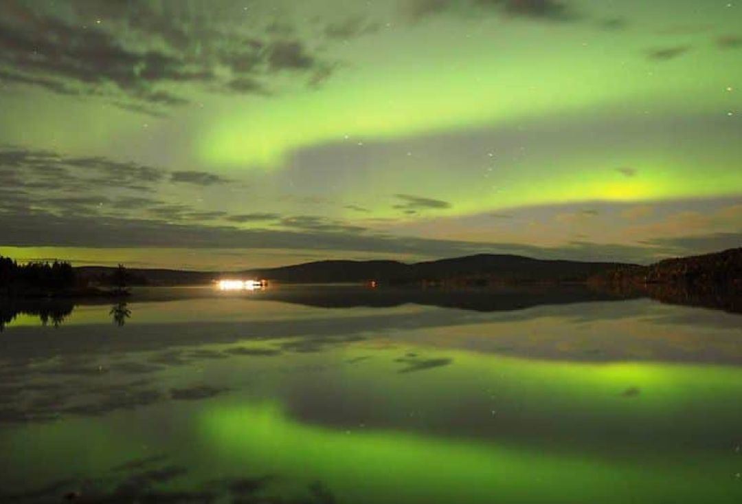 Sädemäiset revontulet heijastuvat tyynen järven pinnasta.