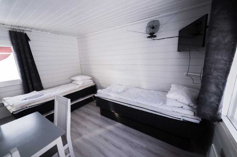 Huone valkoisilla puupaneeleilla ja mustilla tekstiileillä, kahdella yhden hengen sängyllä ja pienellä ruokapöydällä.