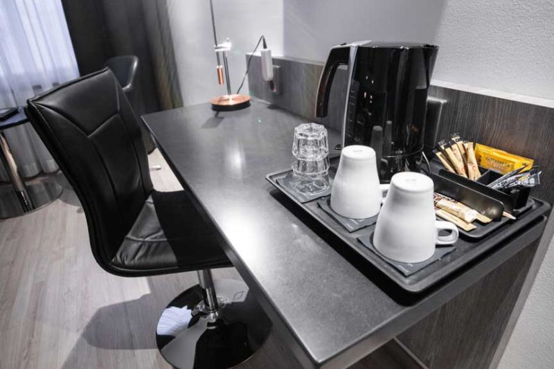 Mustalla tuolilla varustettu sivupöytä, jolla vedenkeitin, kuppeja ja laseja.
