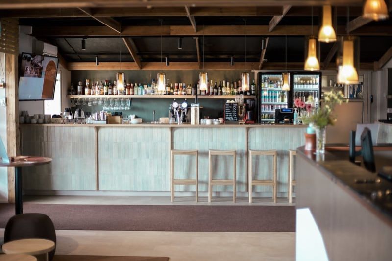 Baaritiskin edessä baarituoleja ja tiskin takana olevalla seinällä paljon pulloja.