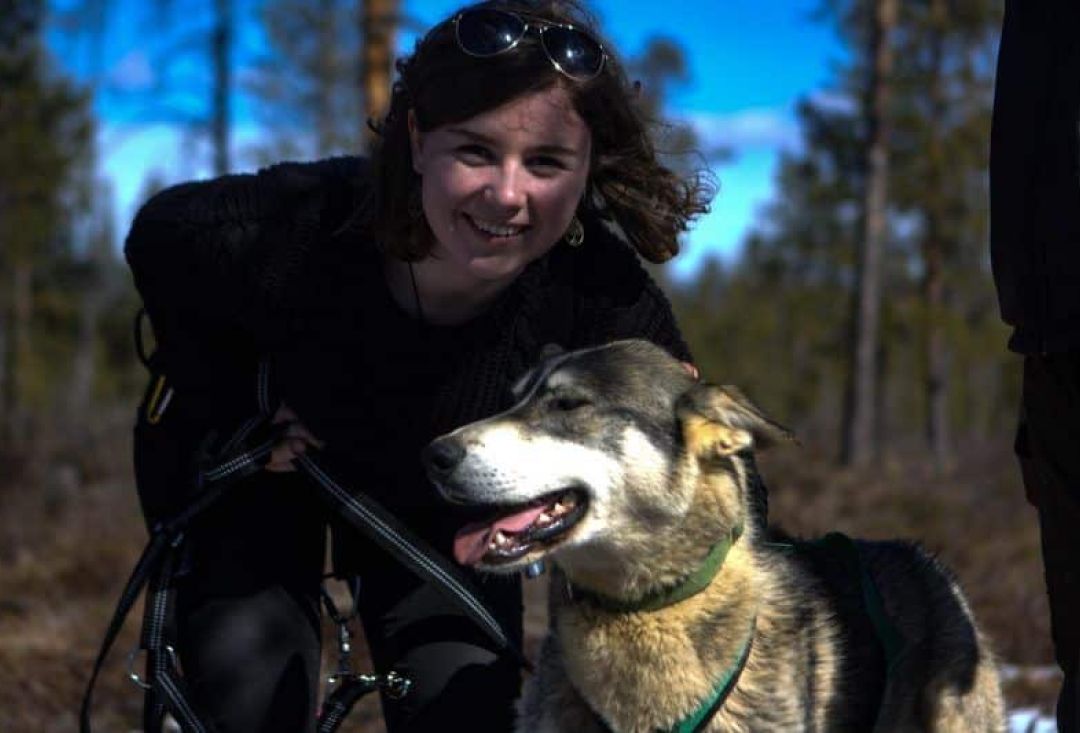 Iloinen nainen kumartuneena huskyn vierelle poseeraamaan.