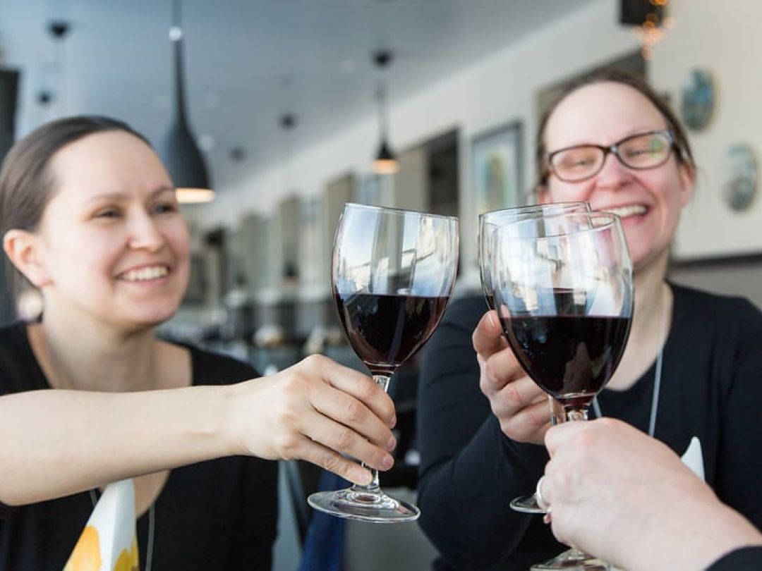 Ihmiset kilistämässä viinilaseja ja hymyilemässä ravintolassa.