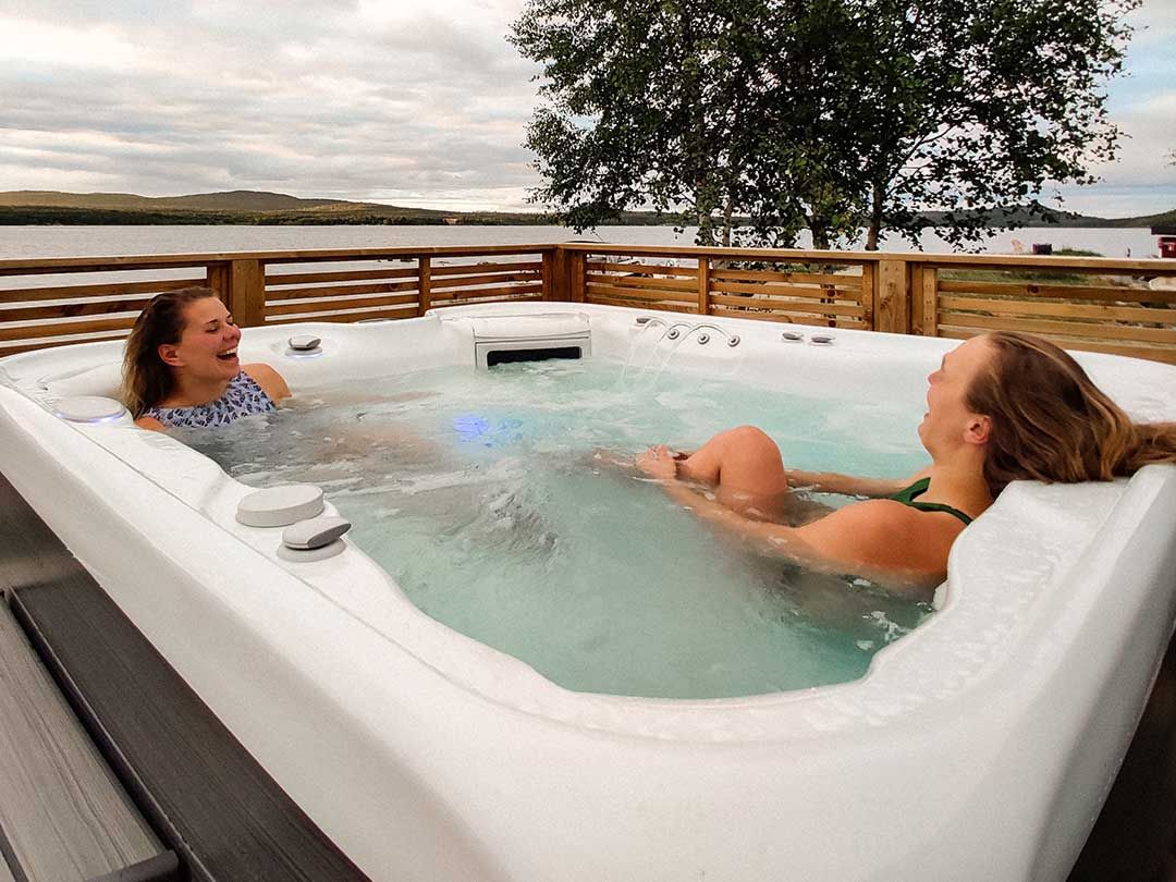 Kaksi naista nauraa ja nauttii ulkoporealtaassa järven lähellä.