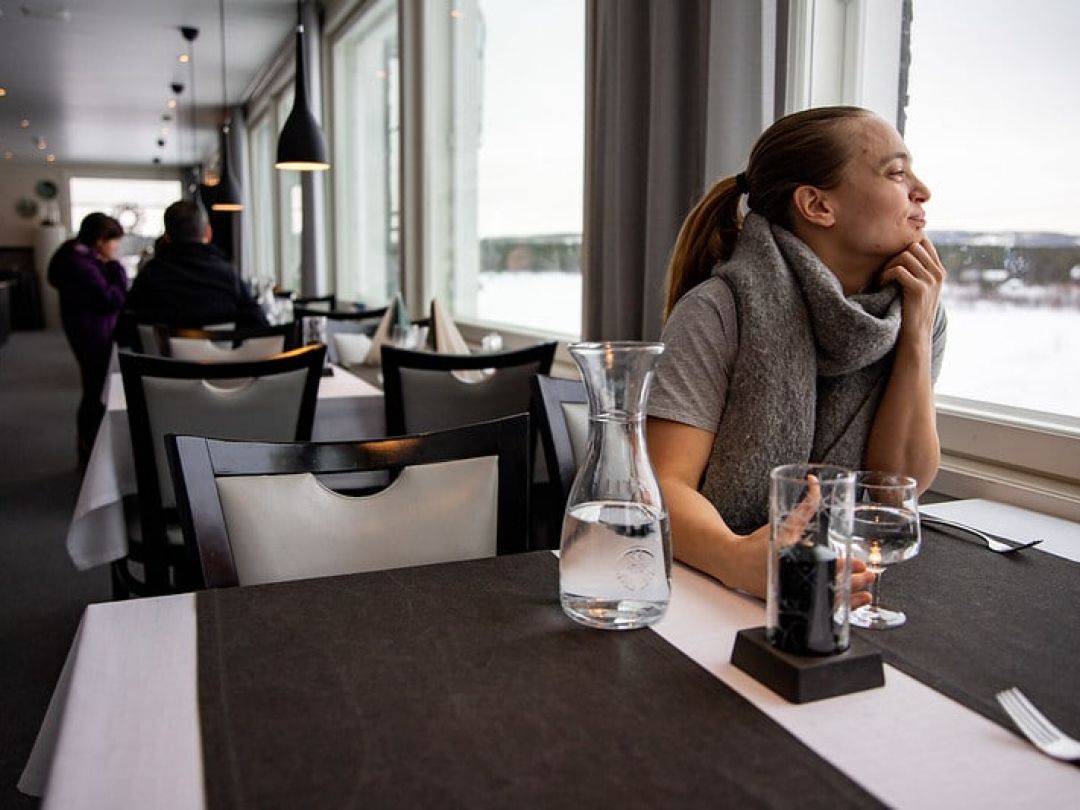 Nainen istumassa ravintolan pöydässä ja katselemassa mietteliäänä ulos ikkunasta.