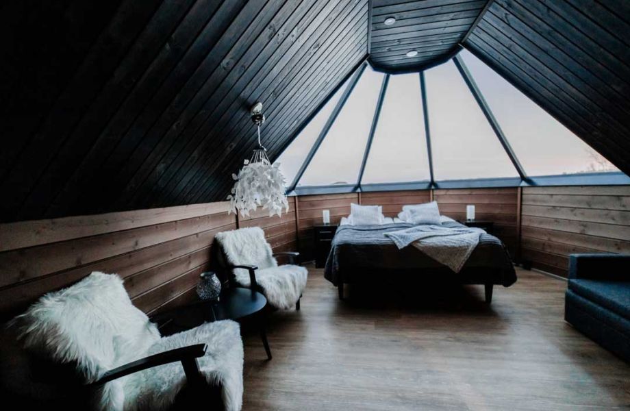 Wooden room with dark ceiling. Double bed and two chairs covered with sheepskin rug.