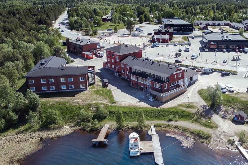 Hotelli Inari ilmakuvana. Suuria rakennuksia rannan läheisyydessä ja taustalla Inarin kylää. Rannassa venesatama.