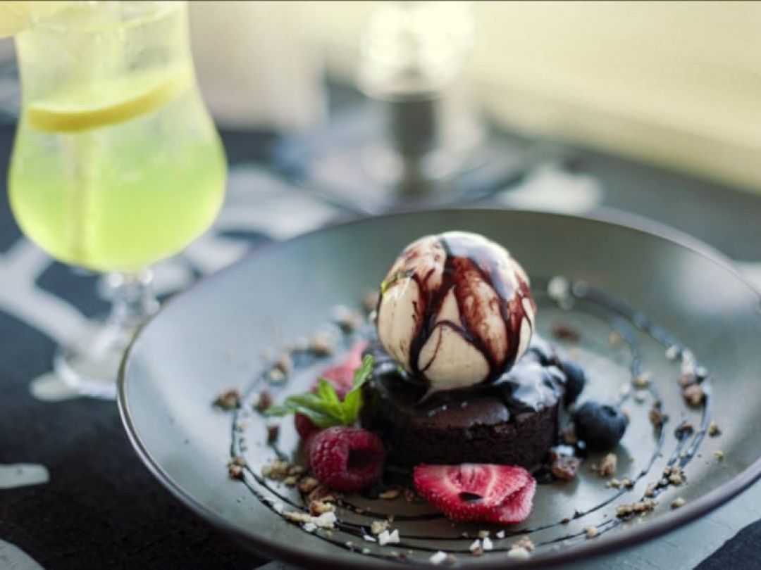 Jälkiruoka jäätelöstä, marjoista ja suklaakastikkeesta lautasella.