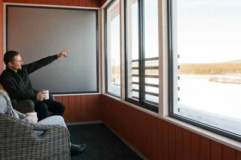 A couple sitting on a glassed balcony watching the views. Man pointing something with finger.