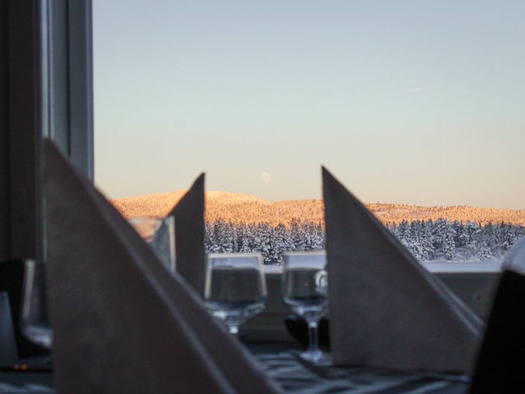 Talvinen maisema lumisista puista ravintolan ikkunasta, pöydällä taitellut lautasliinat.