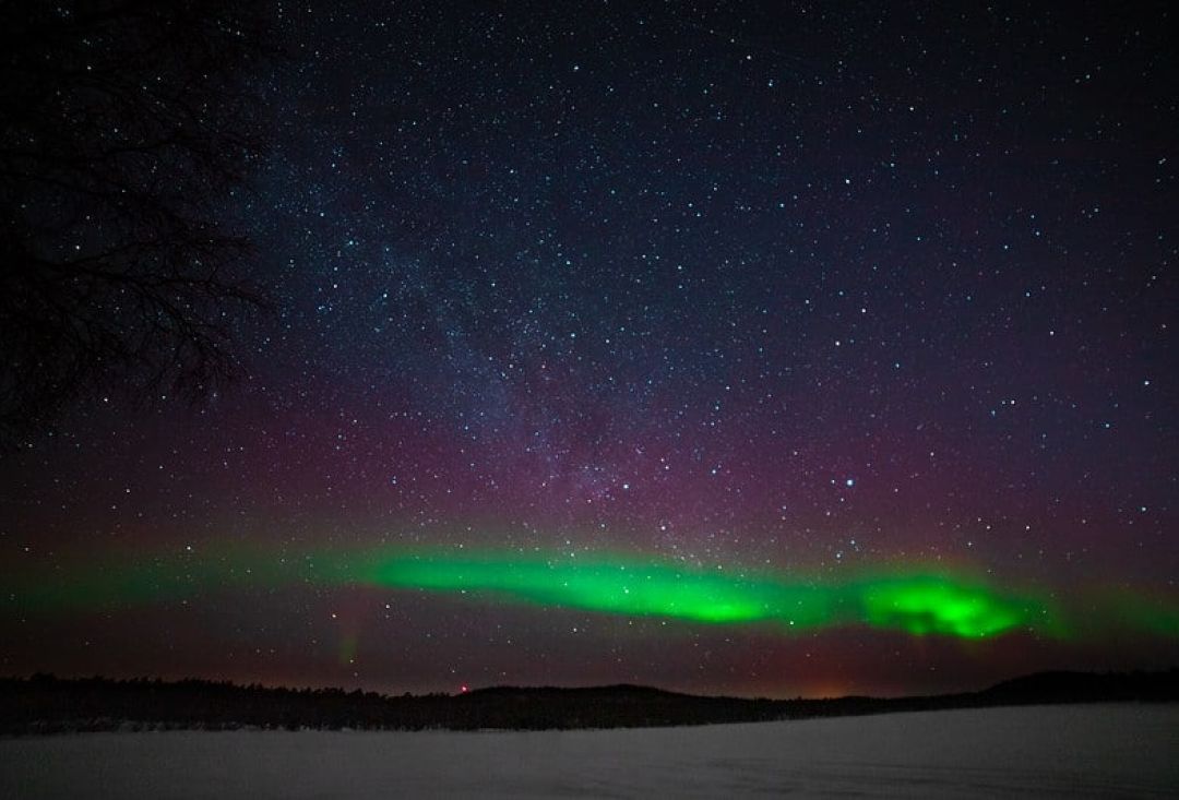 Revontulet kaukaisella taivaanrannalla. Taivas on täynnä pieniä kirkkaita tähtiä.