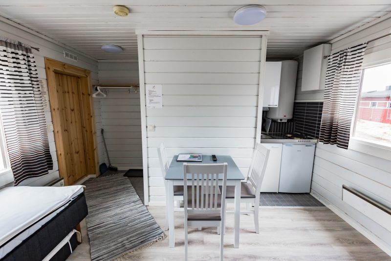 Puupaneloitu huone pienellä keittonurkkauksella, ruokapöydällä.