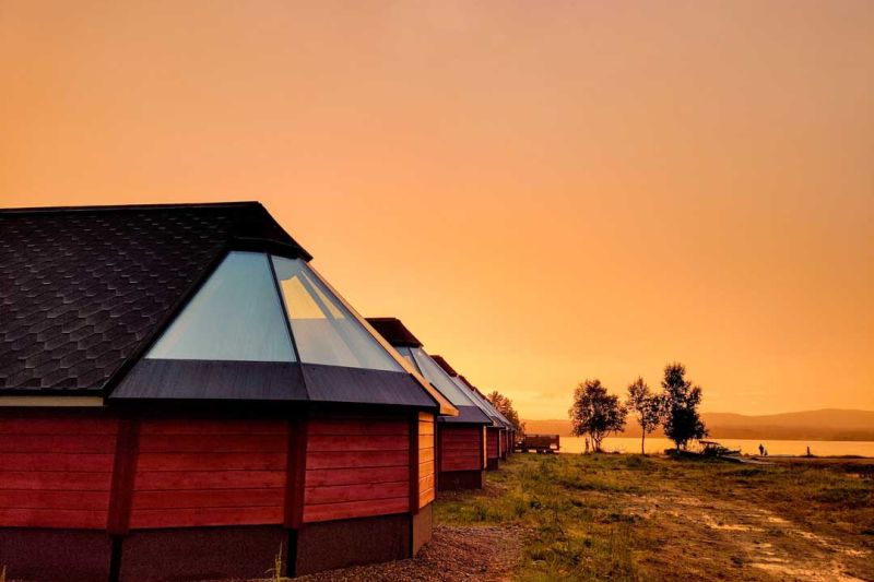 Panoraamaikkunoin varustettuja mökkejä auringonlaskussa.