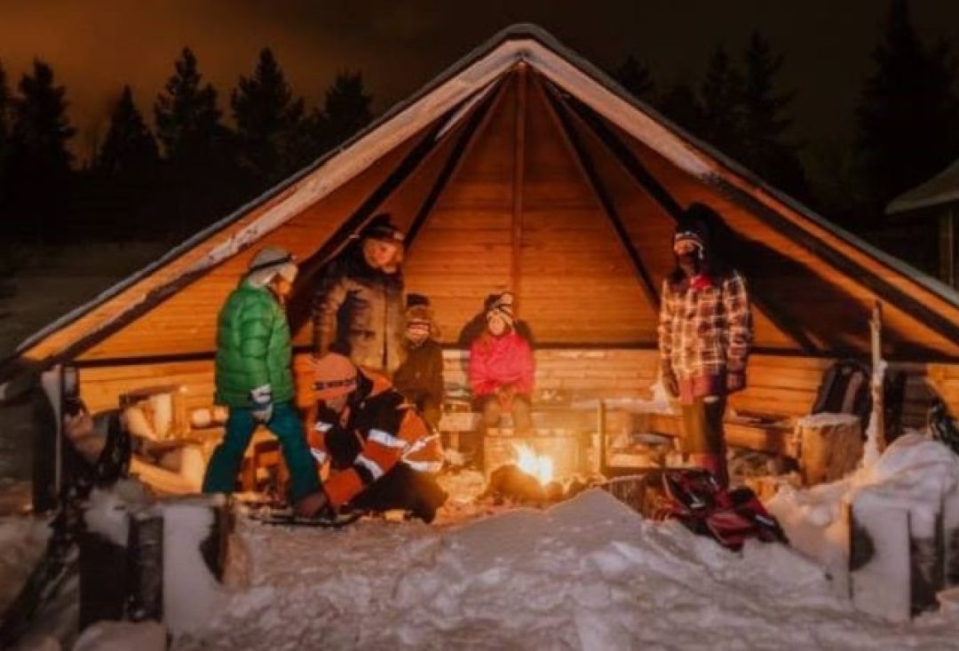 People by the bonfire in half open hut in the dark forest.