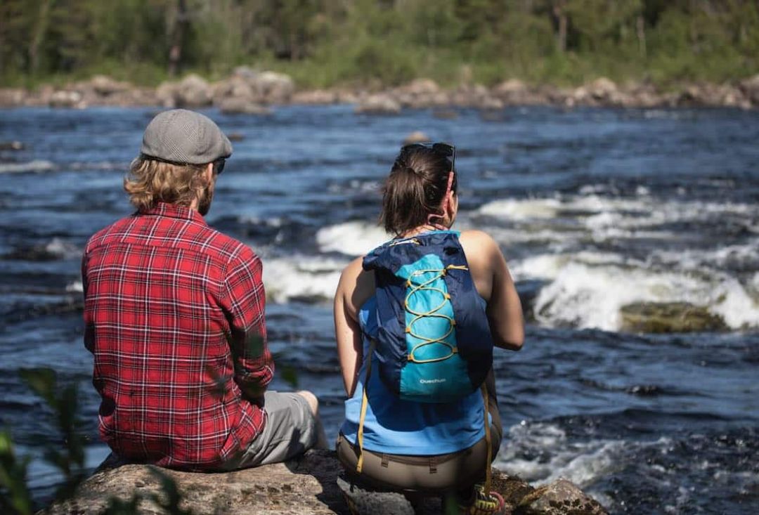 Pariskunta istuu kivellä joenrannassa katselemassa maisemia kirkkaana päivänä.