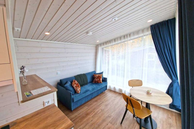 Brightly lighted living room with blue sofa and small round, wooden dining table.