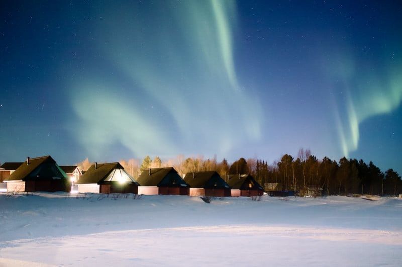 Talvinen maisema mökkien suuntaan, taivaalla revontulet.