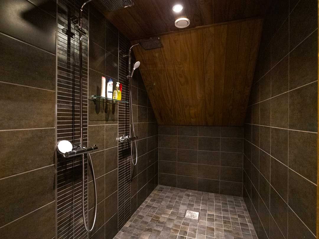 Suihkuhuone kahdella suihkupäällä, moderni laatoitus ja vino katto.