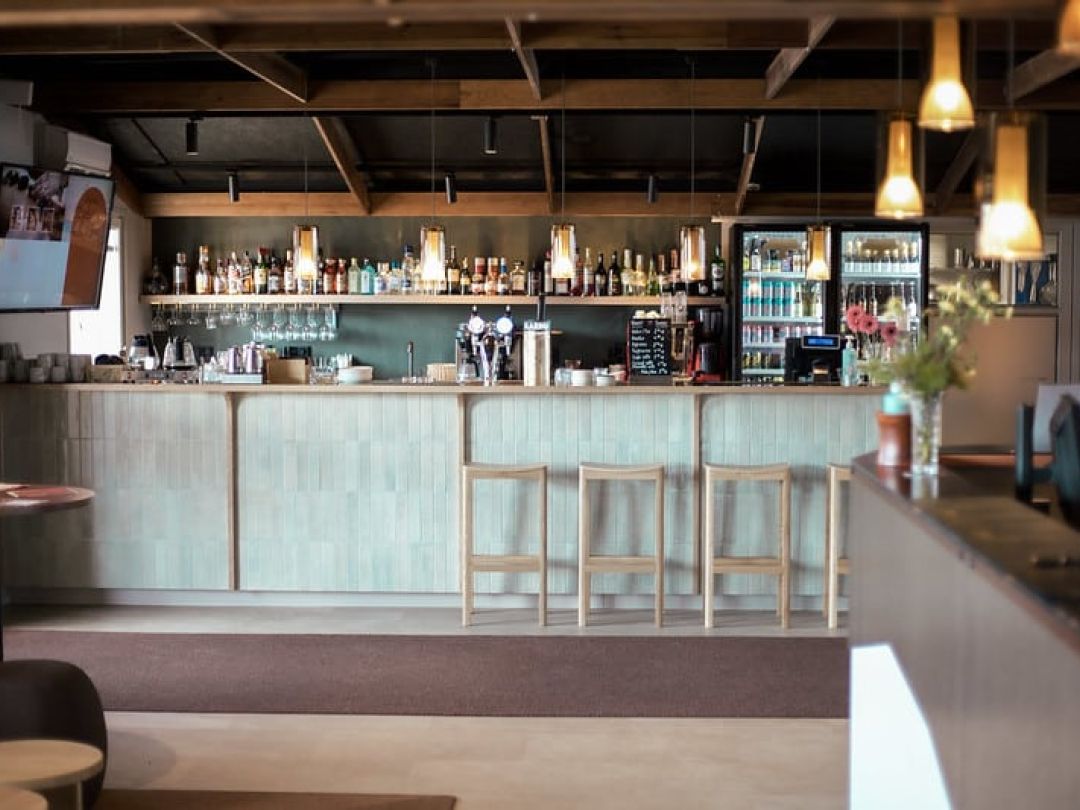 Moderni baaritiski, hyllyillä pulloja ja korkeat tuolit.