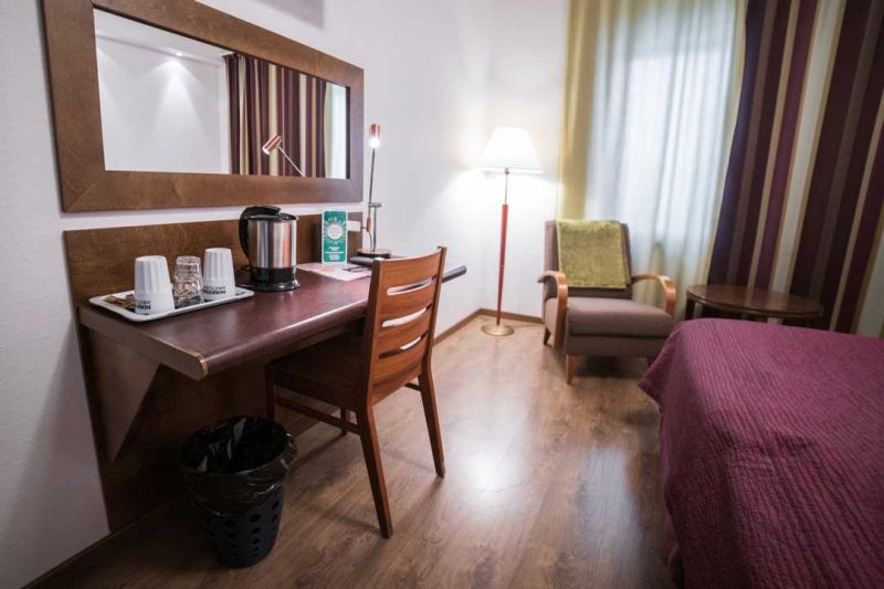 Sivupöytä vedenkeittimellä ja tarjottimella, jossa kuppeja ja laseja. Pöydän yläpuolella pitkä peili.