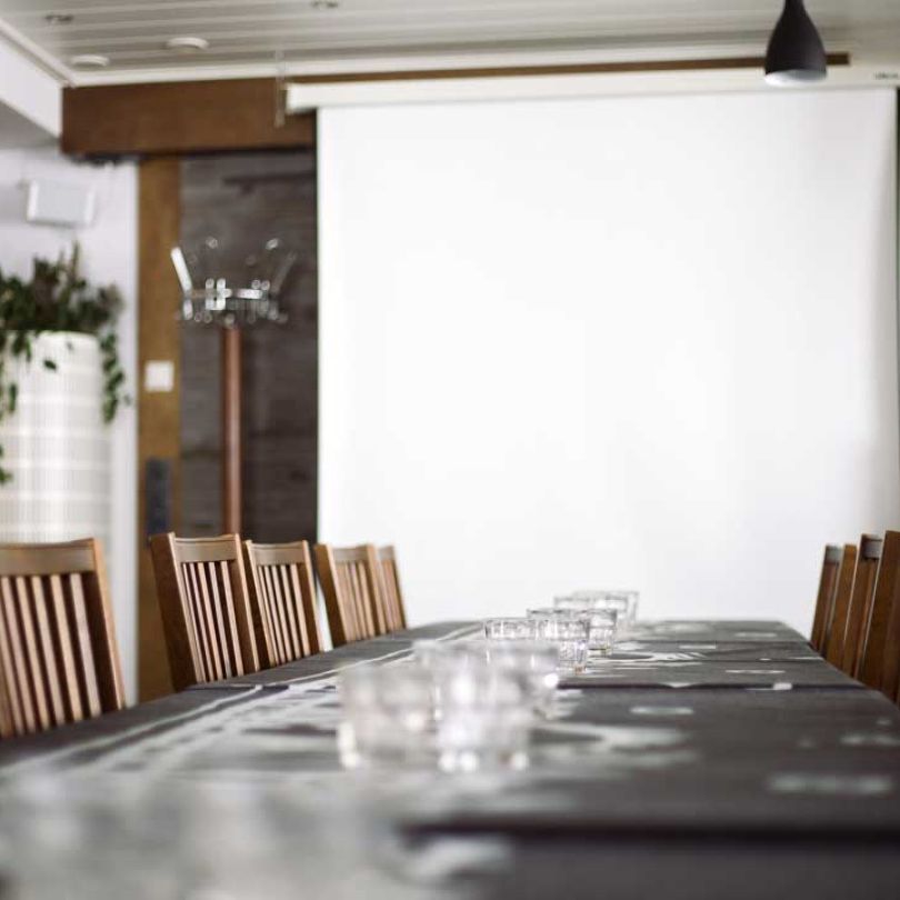 Long table with chairs, glasses on table. White screen in front of table.