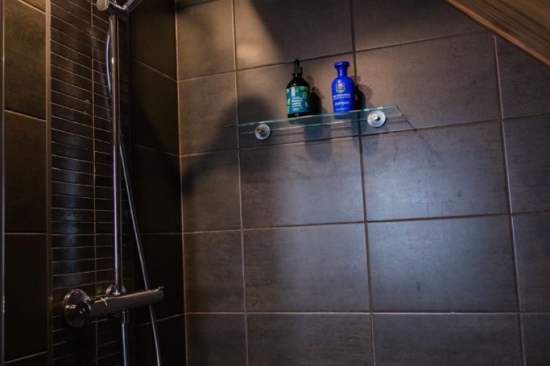 Dark tiled shower corner with large shower head.