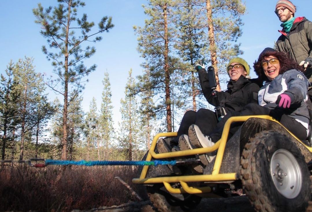 Renkain varustettu reki, jossa ohjastaja takana ja kyydissä kaksi iloista matkustajaa.
