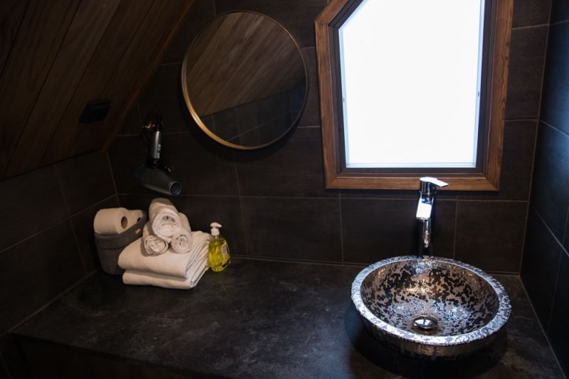 Bathroom counter top with stone  sink and round mirror. Shaped window above the sink.