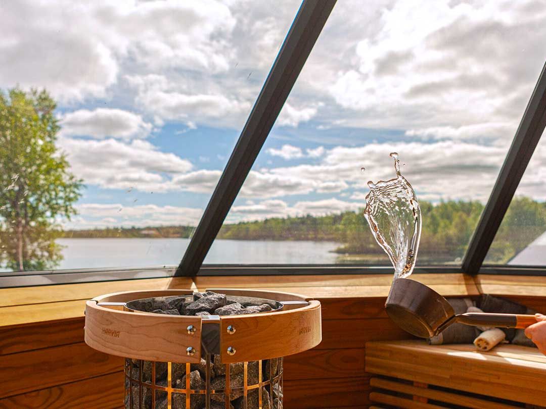 Saunan sisätila kiukaineen ja suuret ikkunat järvimaisemaan.