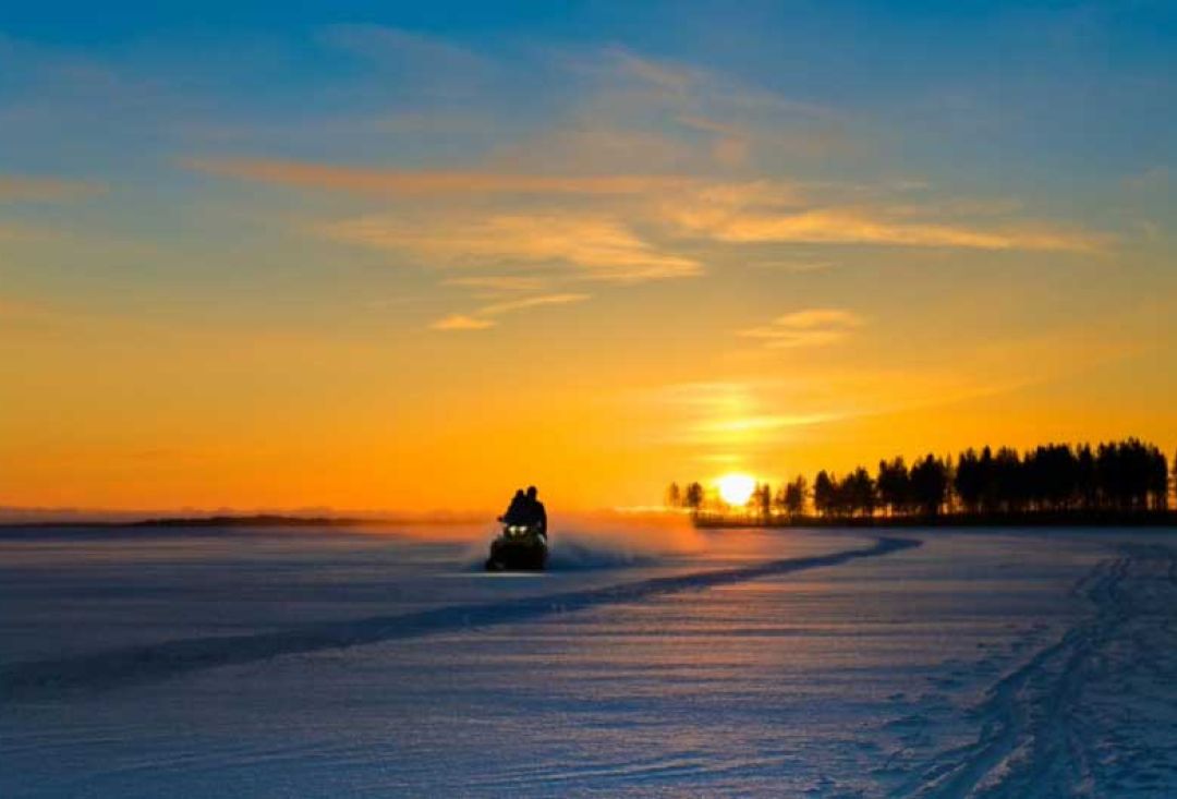 Kelkka ajaa poispäin auringonlaskusta hämärällä järvenjäällä.