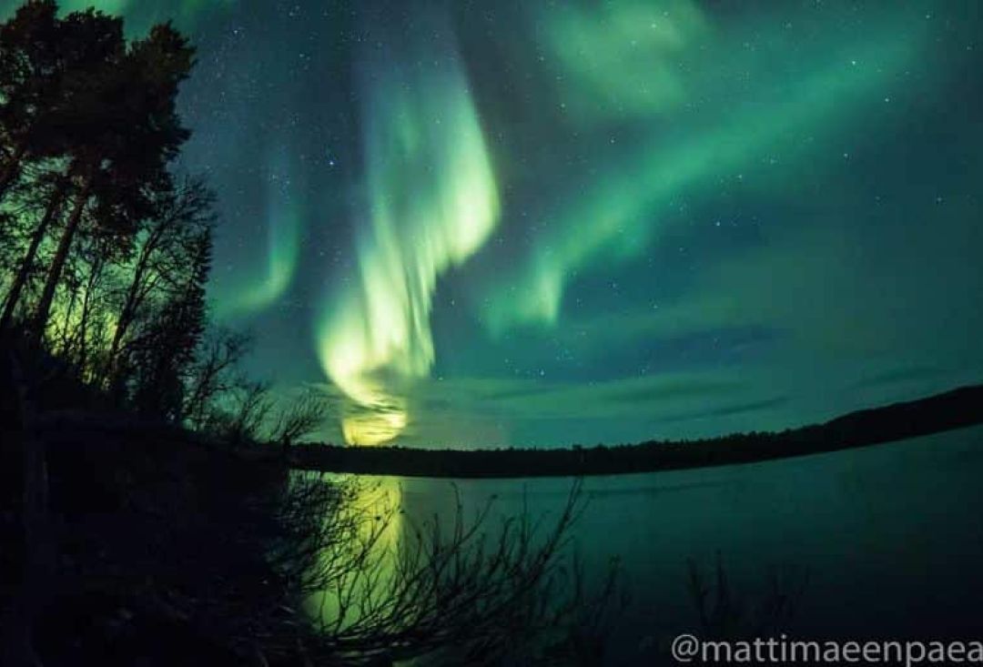 Mutkittelevat revontulet täyttävät öisen taivaan järven yllä.