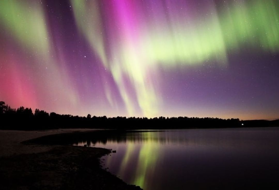 Green and pink northern lights over lake, picture by Pekka Aikio.