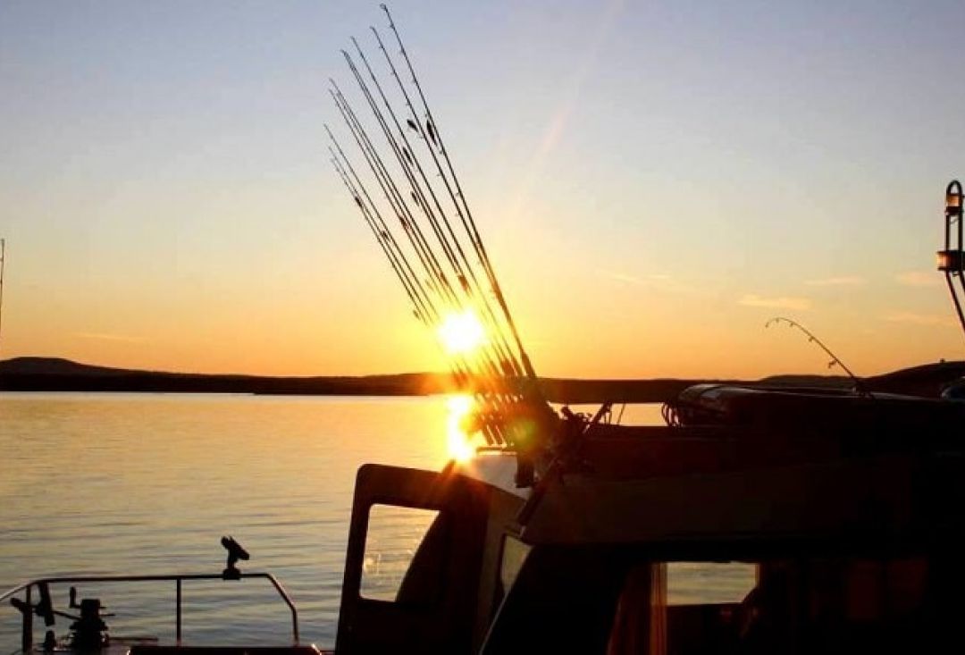 Shadow of fishing boat with rods sticking up from it in sunset.