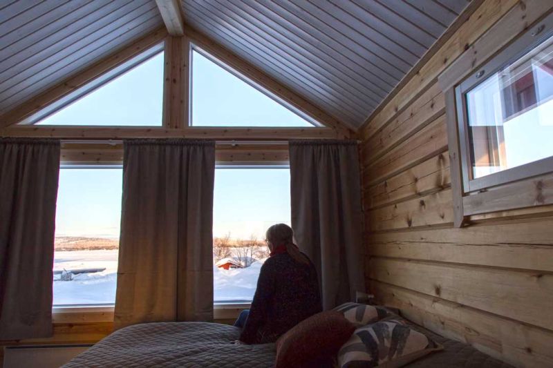 Nainen istuu sängynreunalla katsoen ulos suurista päätyikkunoista.